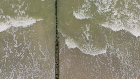 Vista-Aérea-De-Pájaro-De-La-Costa-Del-Mar-Báltico-En-Un-Día-Nublado,-Antiguo-Muelle-De-Madera,-Playa-De-Arena-Blanca,-Grandes-Olas-De-Tormenta-Aplastando-La-Costa,-Cambios-Climáticos,-Gran-Tiro-De-Drones-Avanzando