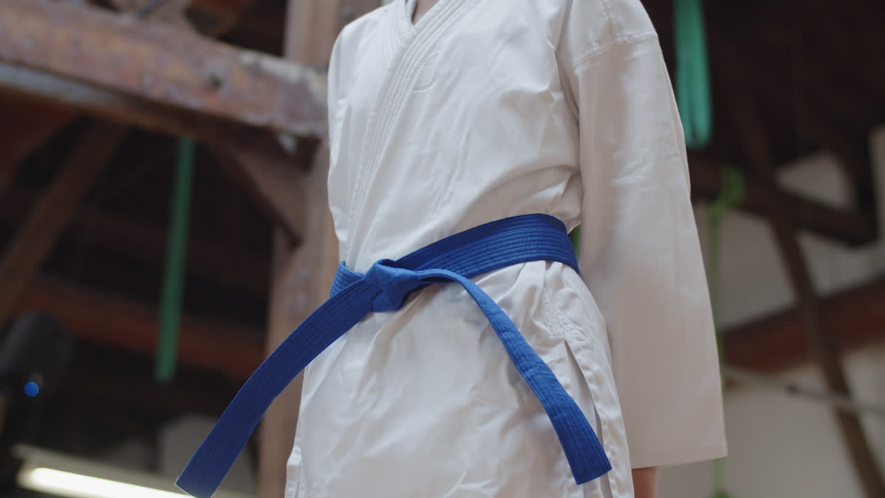 Medium shot of woman tying blue belt on kimono in practice room