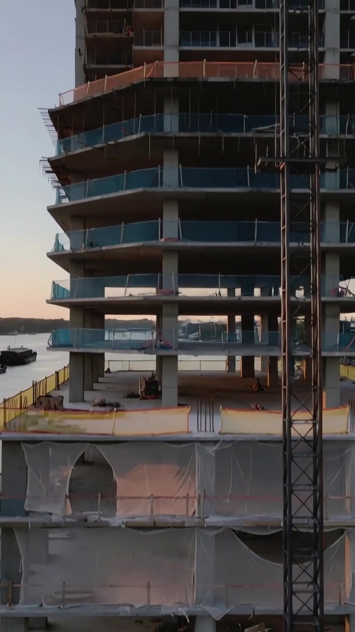 Video vertical: Cámara ascendente revelando un edificio de hormigón en la orilla para mostrar los pisos superiores, grúa.