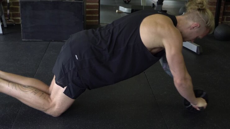 Muscly man in home gym exercising ab roller on floor