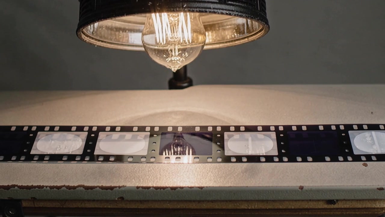 35mm filmstrip glijdt over studiotafel na het trekken, negatieven worden zichtbaar onder Edison-lamp.