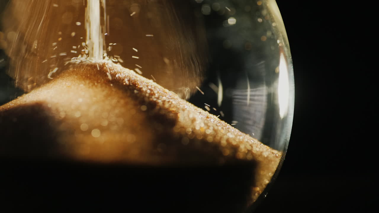 Slow motion video of round hourglass flask where grains of sand fall