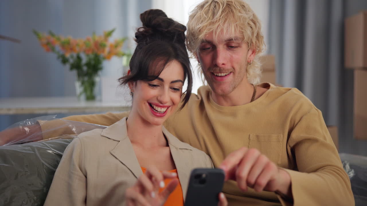 Giovane coppia felice che naviga insieme sullo smartphone nella nuova casa