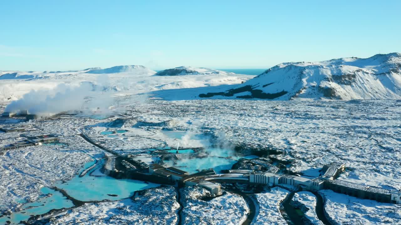 Seen from a high-quality drone, the Blue Lagoon in Reykjavik, Iceland, looks like a beautiful blue pool in the middle of rocky land, with small houses, roads, and pretty scenery nearby