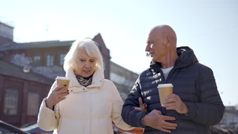 vista frontal de una pareja mayor hablando y caminando por la calle en un día de invierno mientras toma cafés para llevar