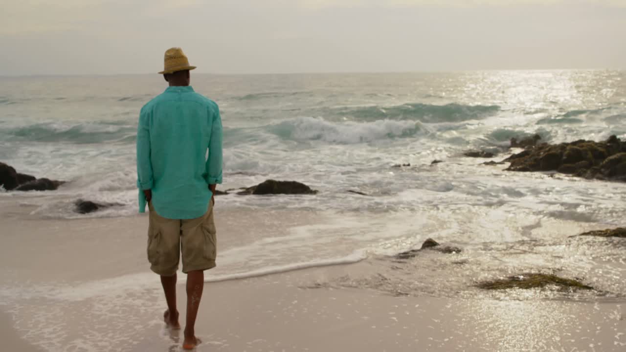 vista trasera de un hombre afroamericano caminando con las manos en el bolsillo en la playa 4k
