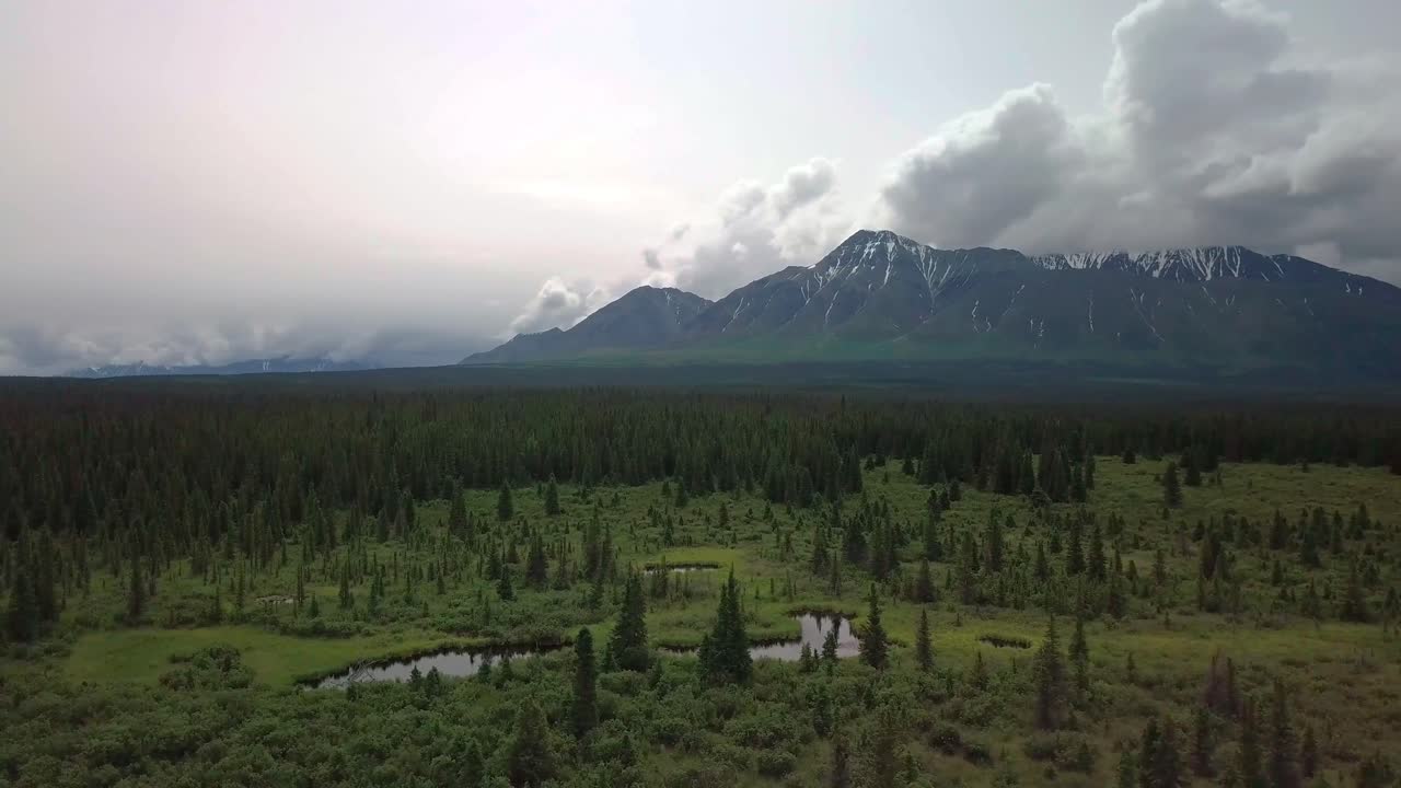 Establishing view of Mount Decoeli pyramidal peak in Yukon Kluane ranges of Saint Elias mountains with bright white sun in cloudy sky, Canada, overhead circle aerial