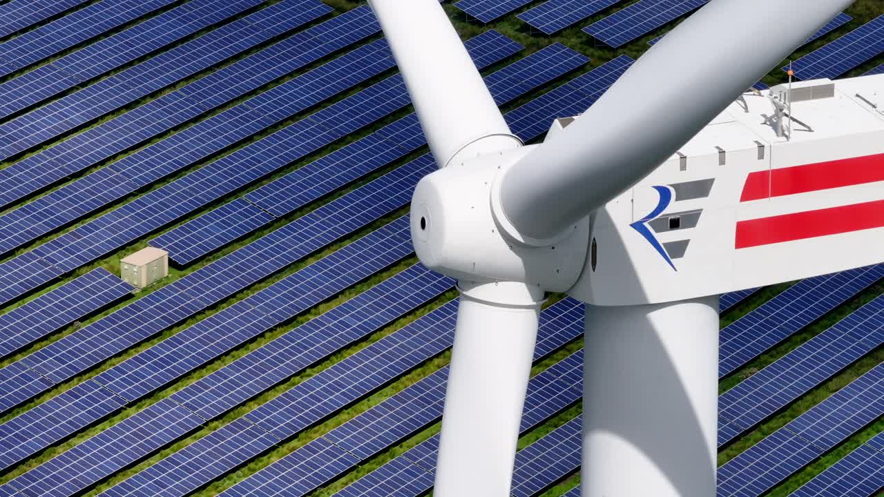 태양광 발전소 한가운데에서 깨 ⁇ 한 에너지를 생산하는 풍력 터빈의 클로즈업 - 배경에서 움직이는 태양광 패널의 파랄락스 효과 - 긴 텔레포토 렌즈