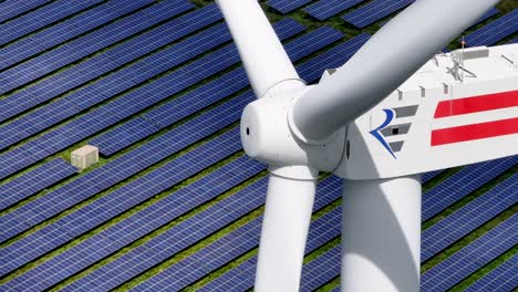 close up of a wind turbine producing clean energy in the midst of a solar farm - parallax effect of solar panels moving in the background - long telephoto lens