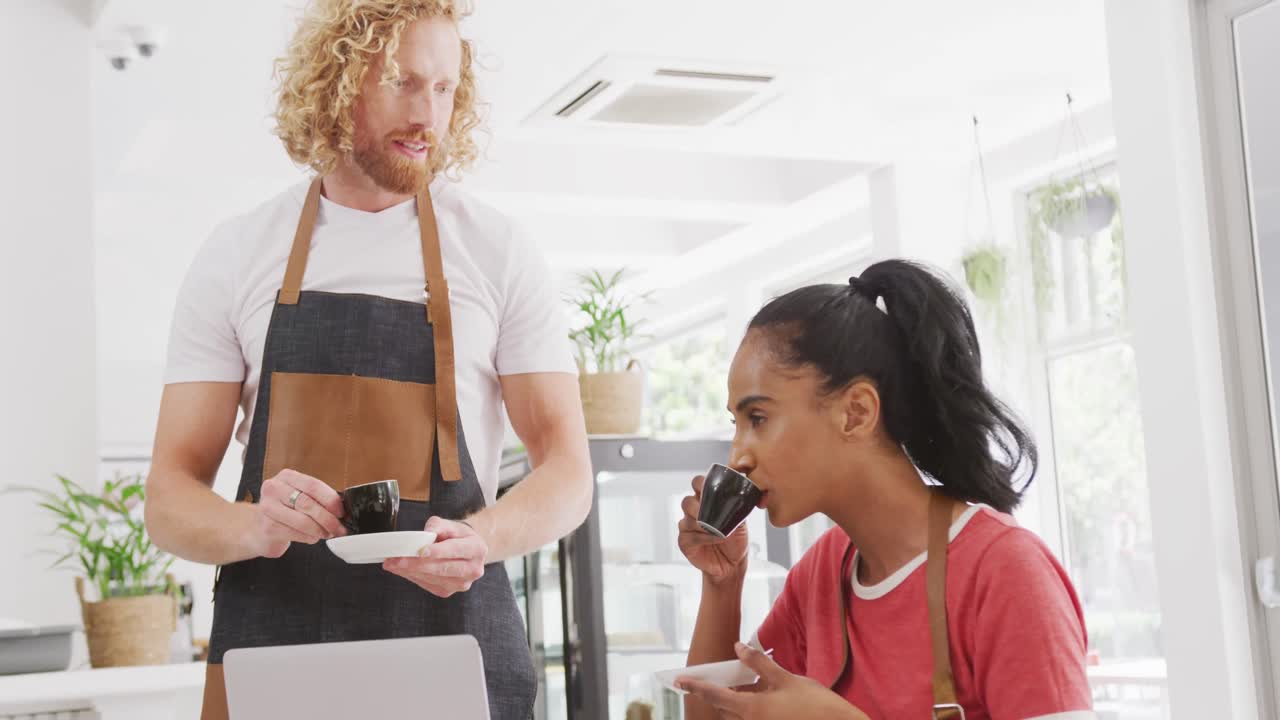 Happy diverse male and female baristas talking and drinking coffee in their cafe