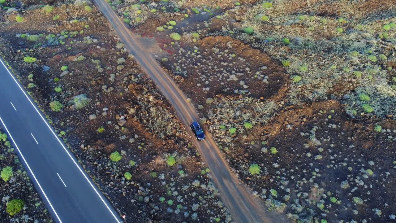 coche oscuro conduciendo en una carretera rural de grava hacia la autopista en lanzarote, vista aérea