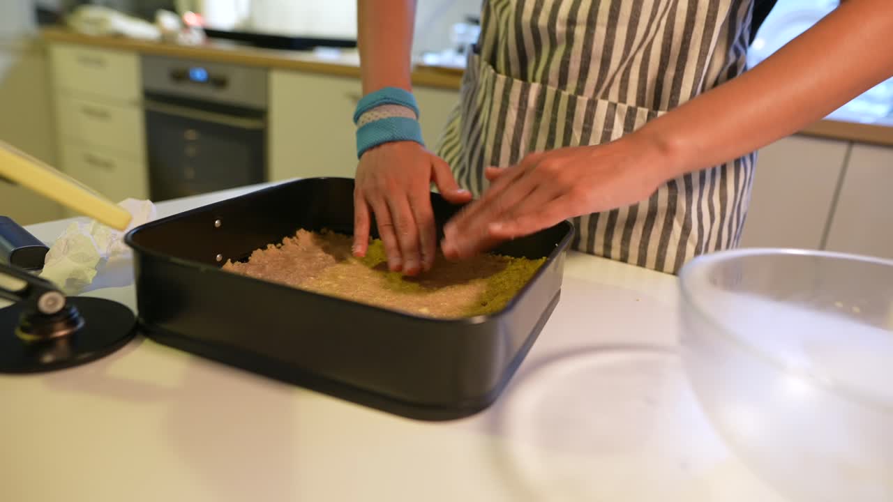 Kvinnehender presser deig i bakeform på kjøkkenet