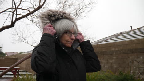 A-beautiful-old-woman-wearing-a-winter-rain-coat-and-hood-staying-warm-in-a-freezing-cold-winter-snow-and-hail-storm-SLOW-MOTION