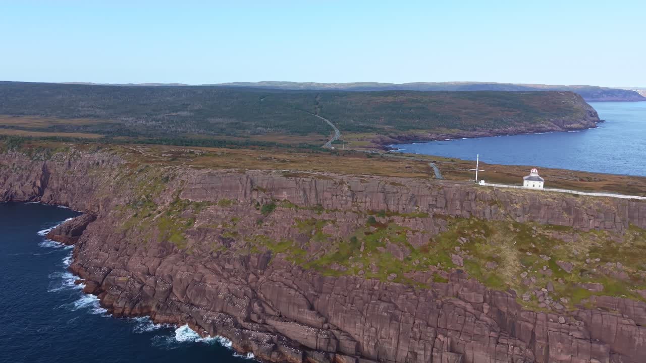 A dramatic aerial sweep along Cape Spear reveals steep cliffs plunging into the Atlantic with Signal Hill visible on the far horizon, filmed from outside the national park border