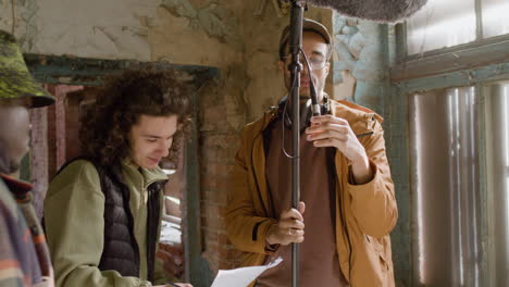 three production coworkers talking while reading a document and holding a microphone during recording of a movie in a ruined building