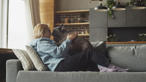 red haired woman caresses her bulldog dog while they are liying on the sofa in the living room at home