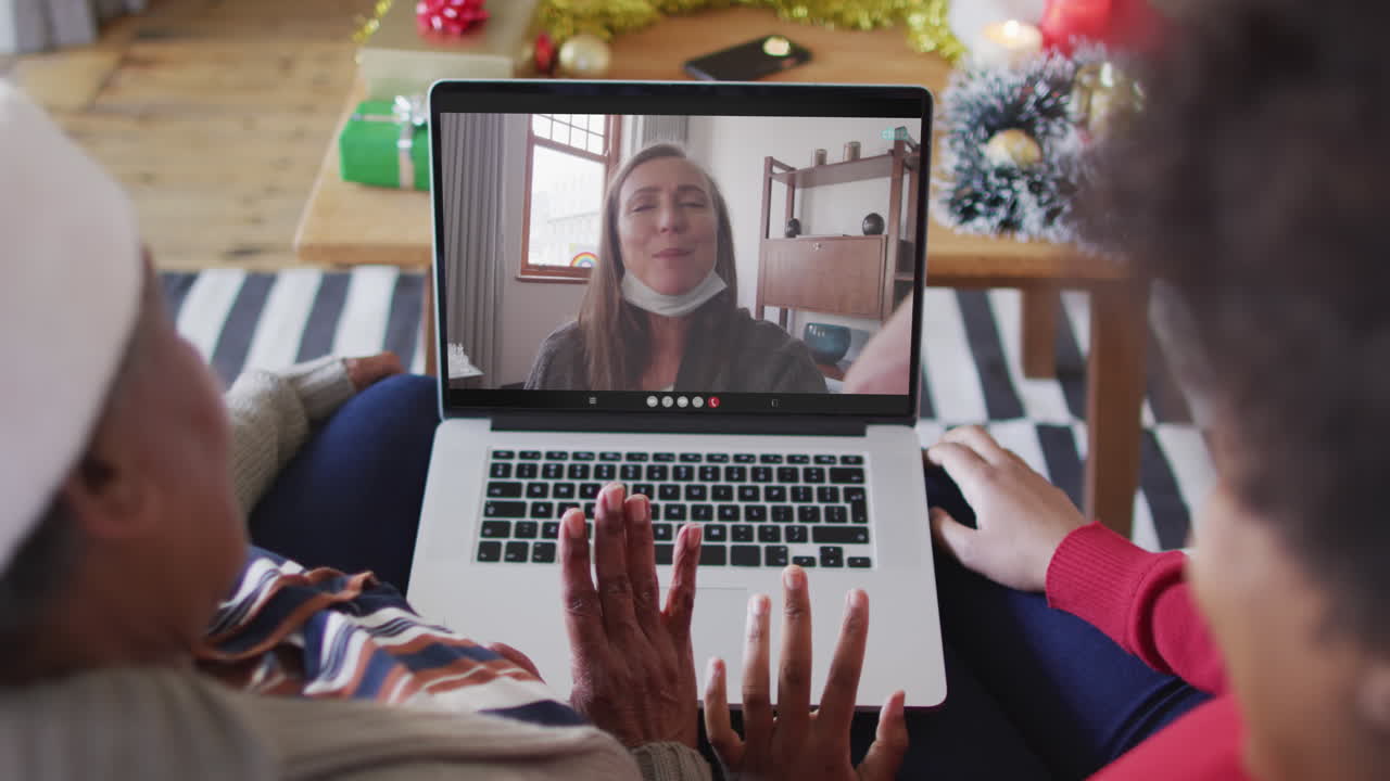 madre y hija afroamericanas usando una computadora portátil para una videollamada de navidad con una mujer en la pantalla