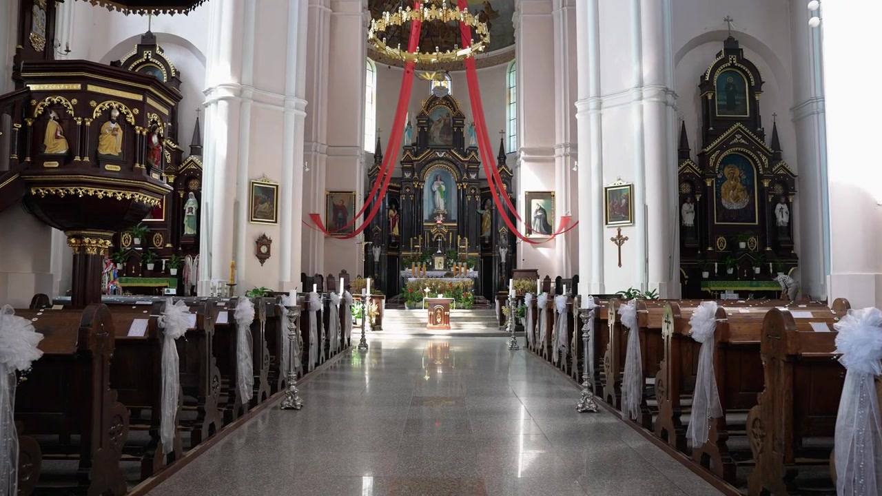 Elegante scatto grandangolare rivela l'altare ornato e illuminato dal sole e i banchi di legno della Chiesa di San Giovanni Battista a Plungė, Lituania. Nessuna persona, luce naturale, architettura gotica dettagliata