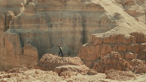 Wide-shot-of-man-walking-over-rugged-rocky-landscape-of-arid-Judean-Desert