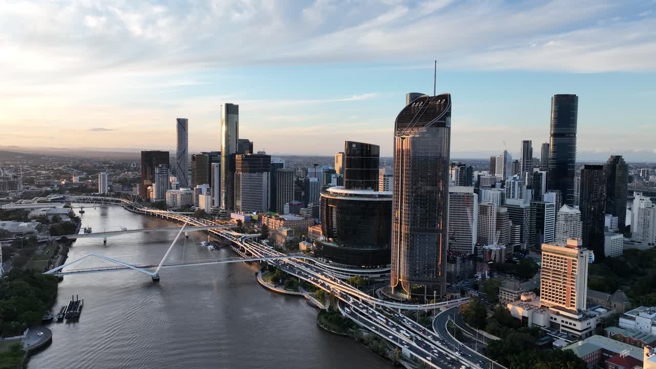 Langsom drone-indzoomning ved den gyldne time langs Brisbane River, der nærmer sig Queens Wharf og The Star Brisbane-tårnene med CBD-skyline bagved, Brisbane, QLD, Australien