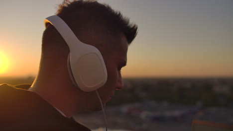 close-up of a man in headphones listening to music on the roof at sunset with a view of the city