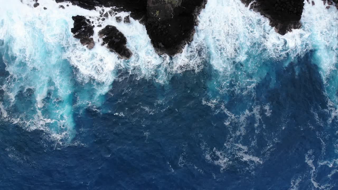 Bird's eye view of pacific waves meeting volcanic black rock cliffs