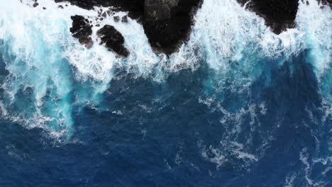 Bird's-eye-view-of-pacific-waves-meeting-volcanic-black-rock-cliffs