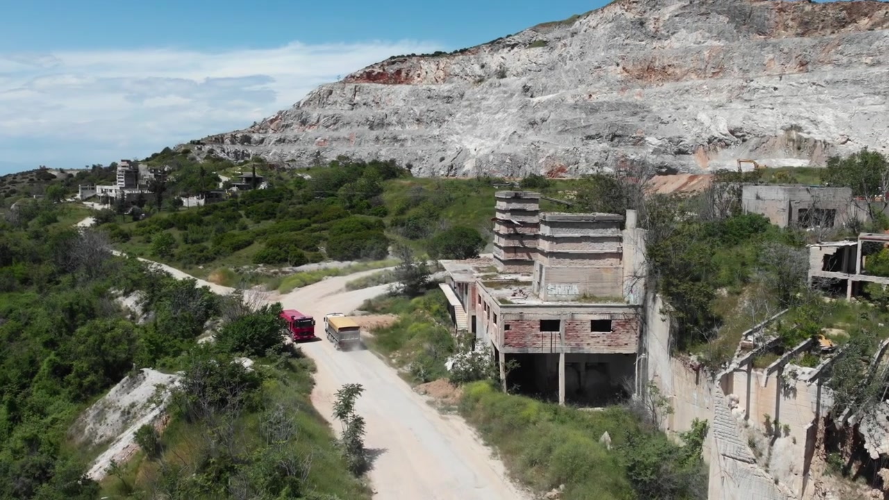 Una cava abbandonata con vecchi edifici e veicoli su una strada sterrata tortuosa. Ideale per documentari sulla storia industriale o sui cambiamenti ambientali.