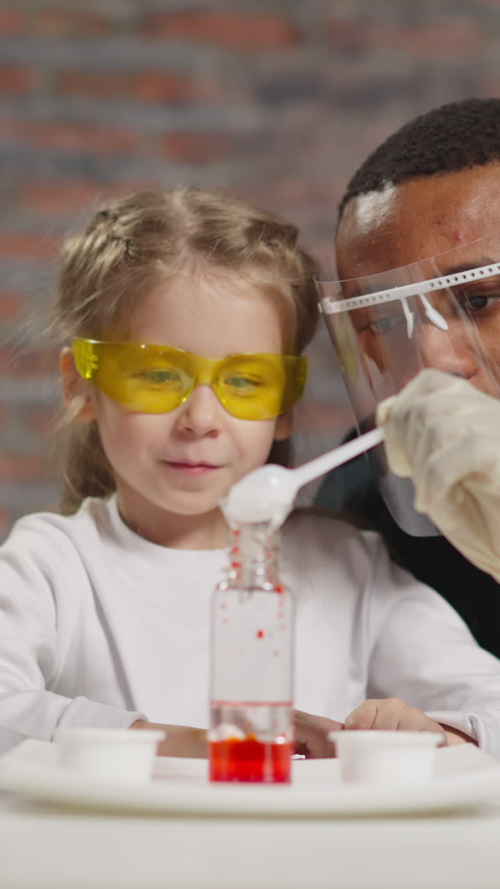Cute little girl talks to Asian chemistry teacher looking at African-American man pouring catalyst powder into bottle in laboratory slow motion