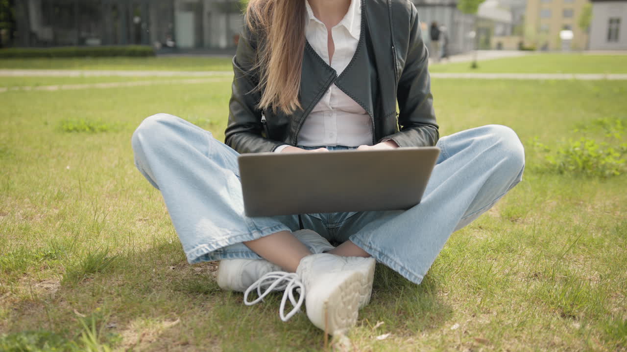 mujer feliz trabajando en una computadora portátil en el césped verde en el parque de verano mujer joven independiente feliz de