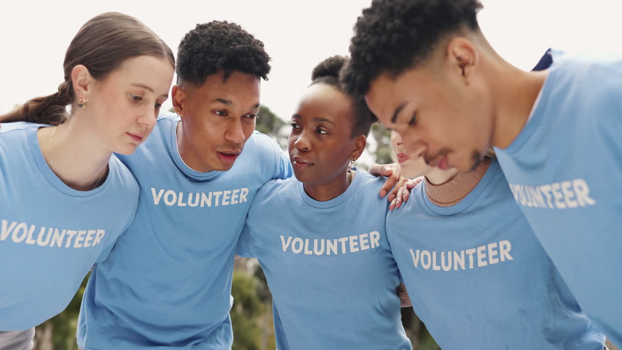 A group of diverse volunteers talking together, smiling and looking happy. They are wearing blue shirts that say 'Volunteer' on them.