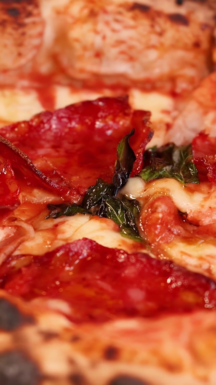 Macro di pizza napoletana con mozzarella fusa, salame e basilico su bordo bruciacchiato