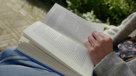 Libro-Abierto-De-Primer-Plano-Mientras-Una-Joven-Lee-En-El-Jardín,-ángulo-Holandés