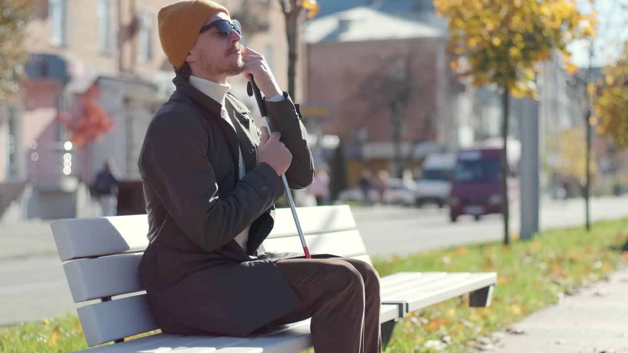 도시 의 공원 의 벤치 에 앉아 있는 스마트폰 을 가진 눈먼 젊은 남자