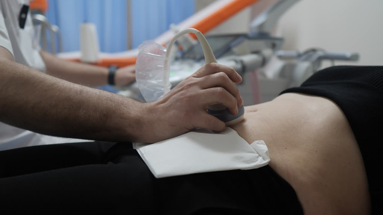 Doctor performing ultrasound on woman's stomach, writes notes during consultation while patient rests on chair