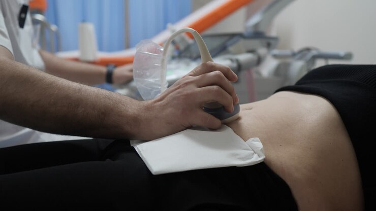 Medico che esegue un'ecografia sull'addome di una donna, prende appunti durante la visita mentre la paziente riposa sulla sedia