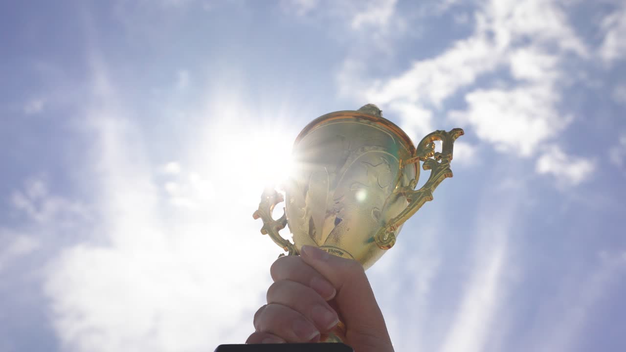 Close-up of a hand holding a trophy against sky background outdoors. Concept of achievement, success, victory, motivation, recognition, and celebration of winning moment