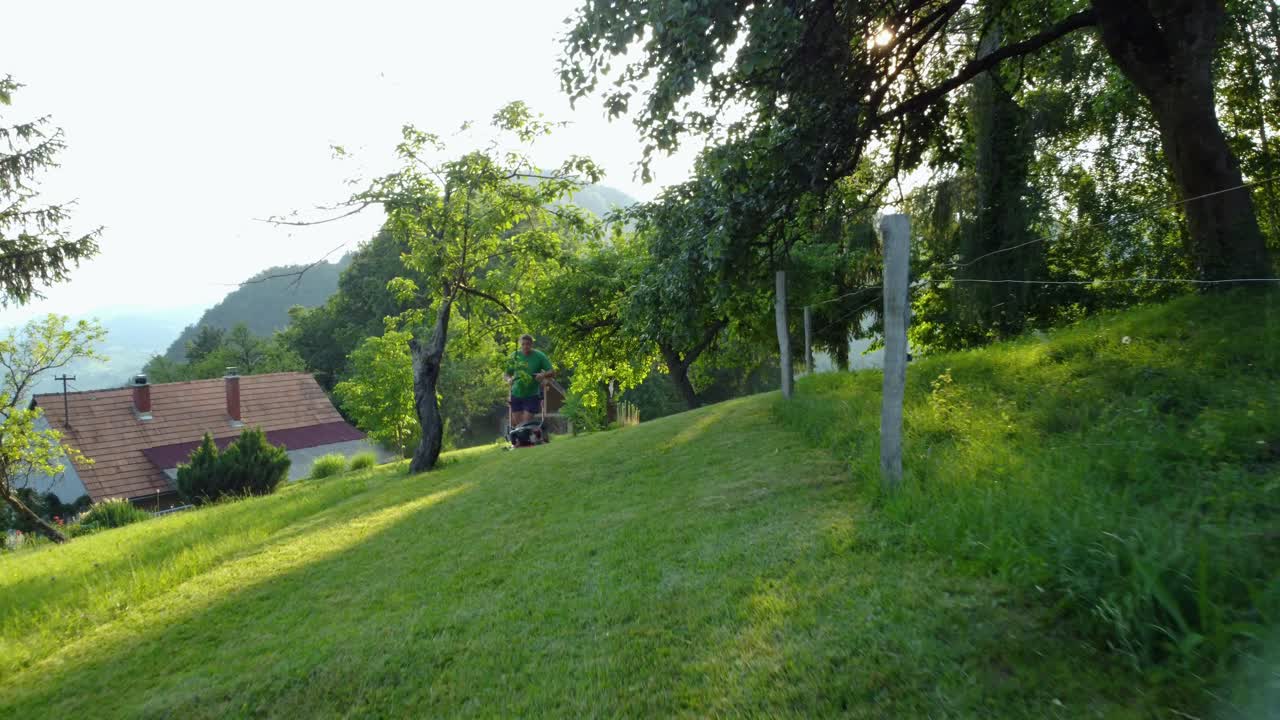반바지와 녹색 셔츠를 입은 남자가 작은 잔디 깎는 기계로 푸른 초원을 깎고 있다