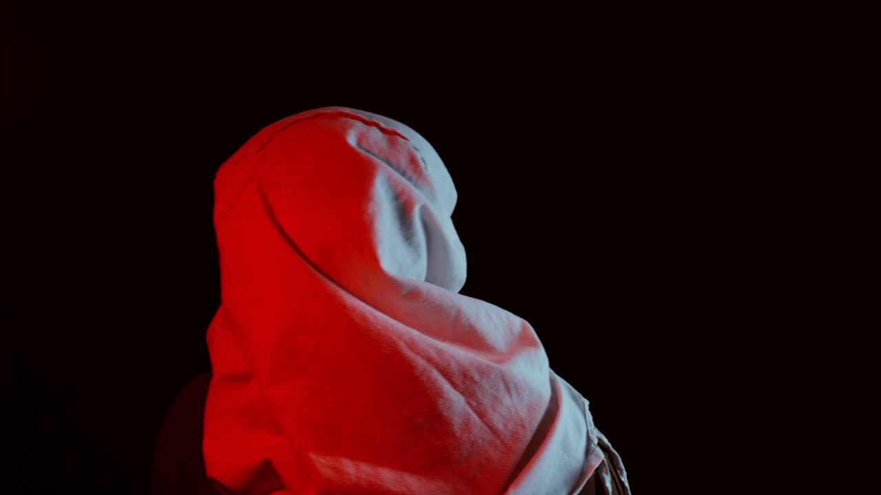 A person with a white cloth covering their head sits in a dark room illuminated by dramatic red and white lighting, creating a tense and cinematic kidnapping atmosphere