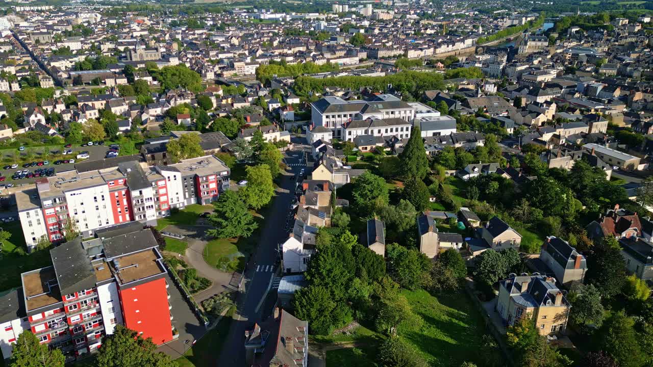 A drone panning shot captures the cityscape of Laval in Mayenne, showing houses, greenery, and trees blending into the urban environment