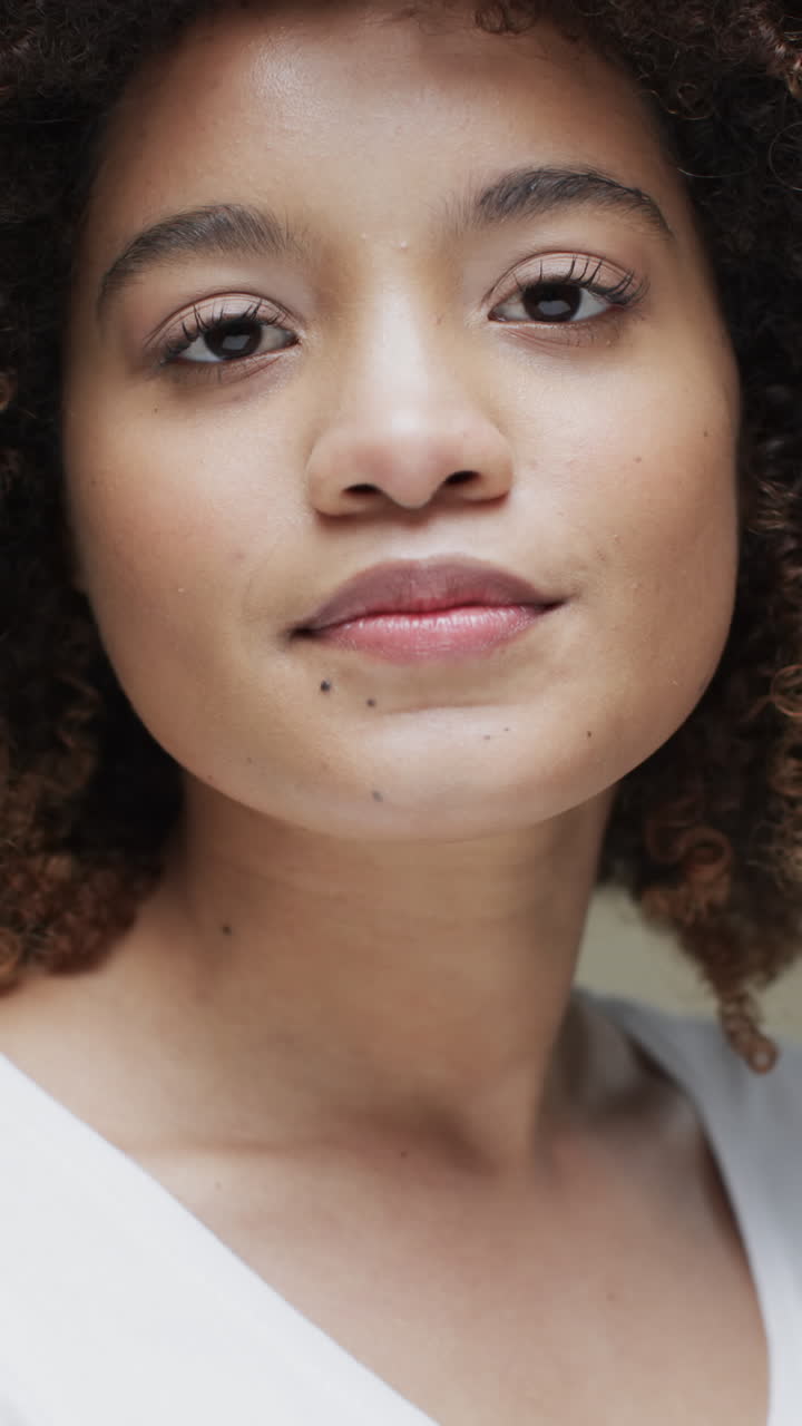Vertical video of biracial woman with dark hair on beige background, slow motion