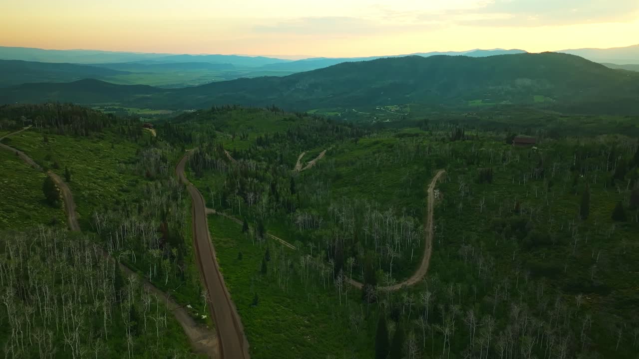 Aerial pullback along roads of forest-lined hills and open terrain in summer near Steamboat Springs, Colorado