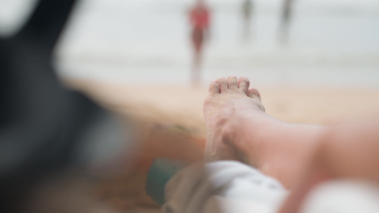 Relaxed toes resting on peaceful sandy shores. Tranquil coastal scene with blurred swimmers and soothing atmosphere. Calm beach setting where gentle waves meet sandy toes and peaceful surroundings