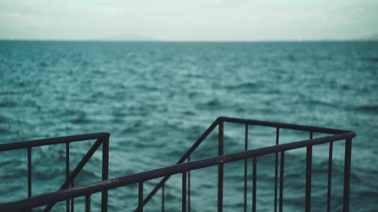 일본 시가의 흐릿한 배경에서 파동이 있는 바다 옆 강철 난간의 선택적 초점 샷 - 슬로우 모션