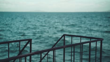 selective focus shot of steel railing by the sea with wave motion in the blurry background in shiga, japan - slow motion