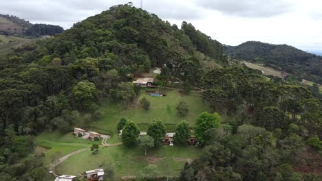 Movimiento-Circular-Con-Drone-Filmando-Una-Montaña-Con-Casitas-En-Medio-De-La-Naturaleza