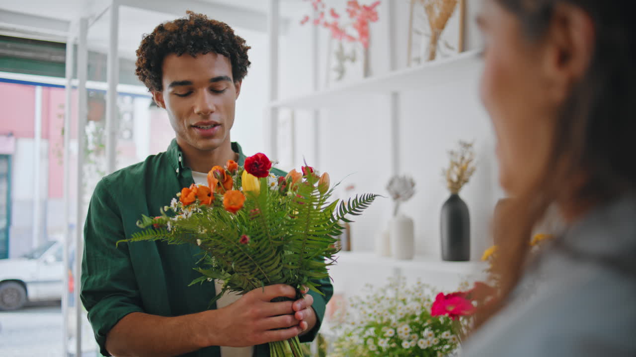 Uomo africano sognante annusa una composizione floreale. Giovane uomo si gode un bouquet di fiori.