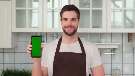 un hombre con un delantal sostiene un teléfono inteligente con una pantalla verde en la mano. aplicación de entrega a casa