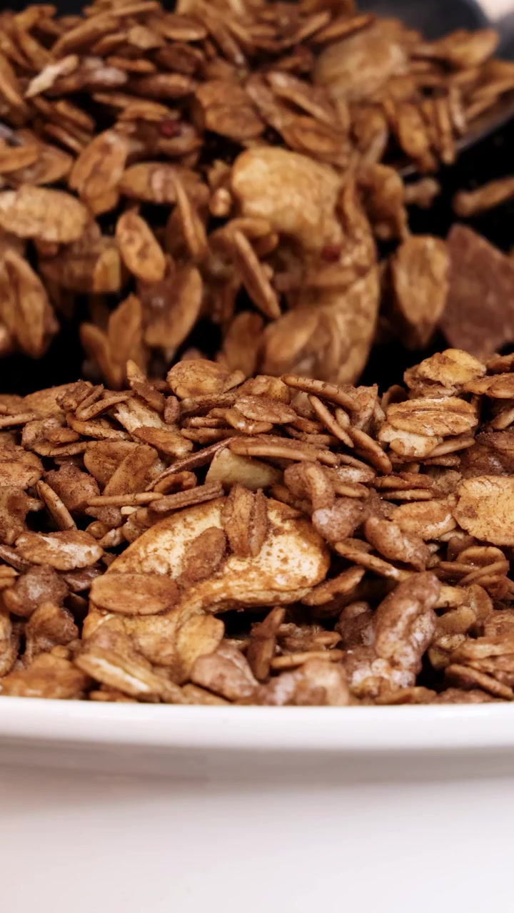 Un cucchiaio rilascia granola in una ciotola, su sfondo nero, evidenziando la consistenza e il movimento