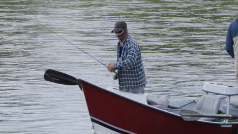 fly fisherman tangles fishing line on small boat on river. static shot.